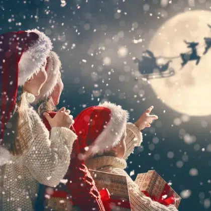 Merry Christmas and happy holidays! Cute little children with xmas presents. Santa Claus flying in his sleigh against moon sky. Kids enjoying the holiday with gifts on dark background.