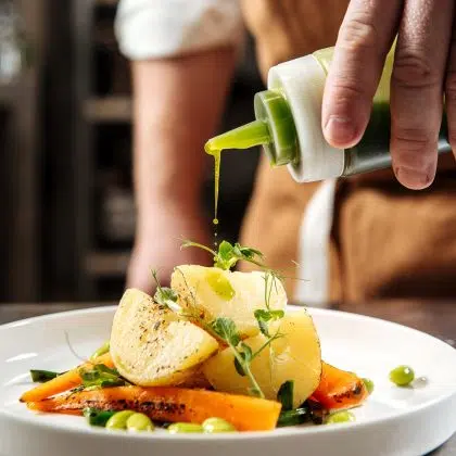 Chef's hands pouring gourmet healthy dish with green sauce