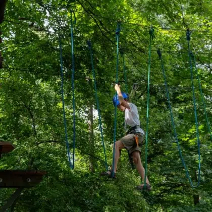 Accrobranche 4 Boy in helmet doing rope course on tree in forest with focused expression on sunny day. Concept of adventure, outdoor activities, and physical fitness. High quality photo
